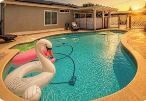 Una piscina con flotadores de cisne e pato inflables, una manguera y una silla de descanso.