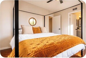 A bedroom with a bed, a round mirror, and a door leading to another room.