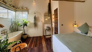 Un dormitorio moderno con una cama grande, suelo de madera, una bañera y varias plantas.