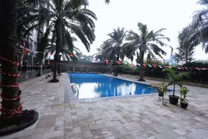 A swimming pool area with palm trees, potted plants, and a tiled walkway.