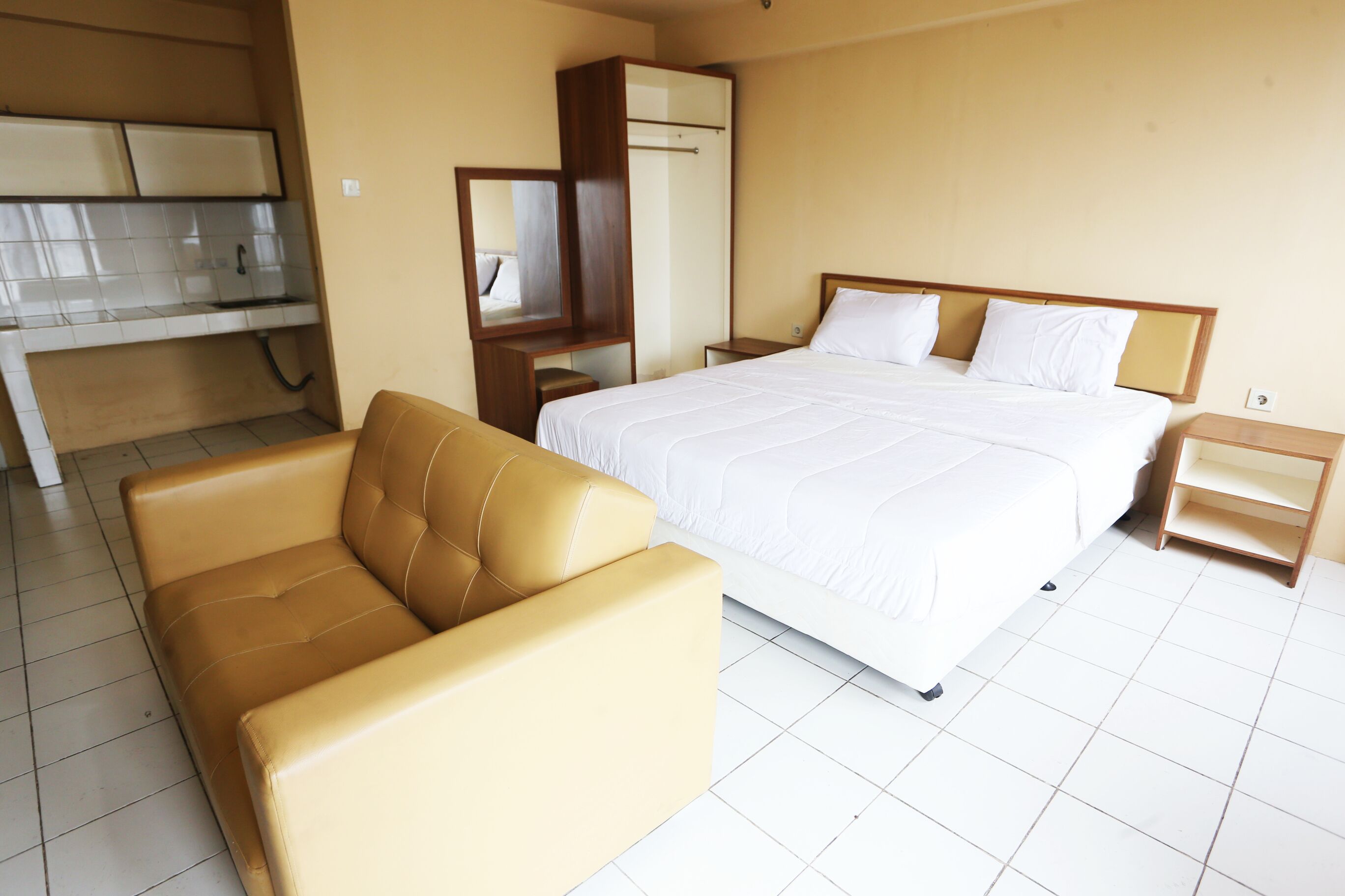 A hotel room with a bed, a sofa, a wardrobe, a desk, and a kitchenette.