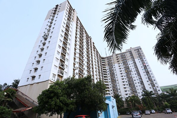 A high-rise residential building with multiple balconies and a parking area in front.