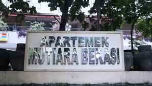 Een bord met de tekst 'APARTMENT MUTIARA BERKASI', met een stenen voetstuk en plantenbakken eromheen.