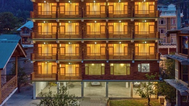 A multi-story wooden building with balconies, large windows, and a visible ground floor area. - Hotel Swastik Grand (Manali)