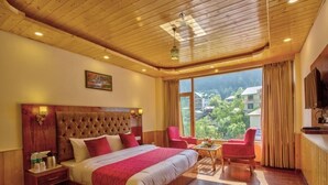 A hotel room with a large bed, wooden flooring, a view of the mountains, and a television on the wall. - Hotel Swastik Grand (Manali)
