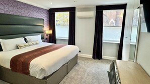 Habitació d'hotel amb un llit gran, un escriptori i una finestra amb cortines.