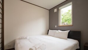 Ein ordentlich bezogenes Bett mit weißen Leinen und aufgerollten Handtüchern, ein dunkles Kopfteil und ein Fenster mit Blick auf Bäume.
