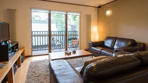 Ein Wohnzimmer mit einer Couch, einem Couchtisch und einem Fernseher. Eine Glasschiebetür führt zu einem Außenbereich mit einem Balkon.