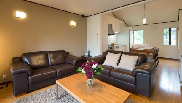 Ein modernes Wohnzimmer mit einer dunkelbraunen Ledersofa, einem Holztisch mit Blumenvase und einer Küche im Hintergrund.