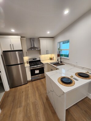 Een koelkast, een oven, een kookplaat, kookgerei, borden en bestek