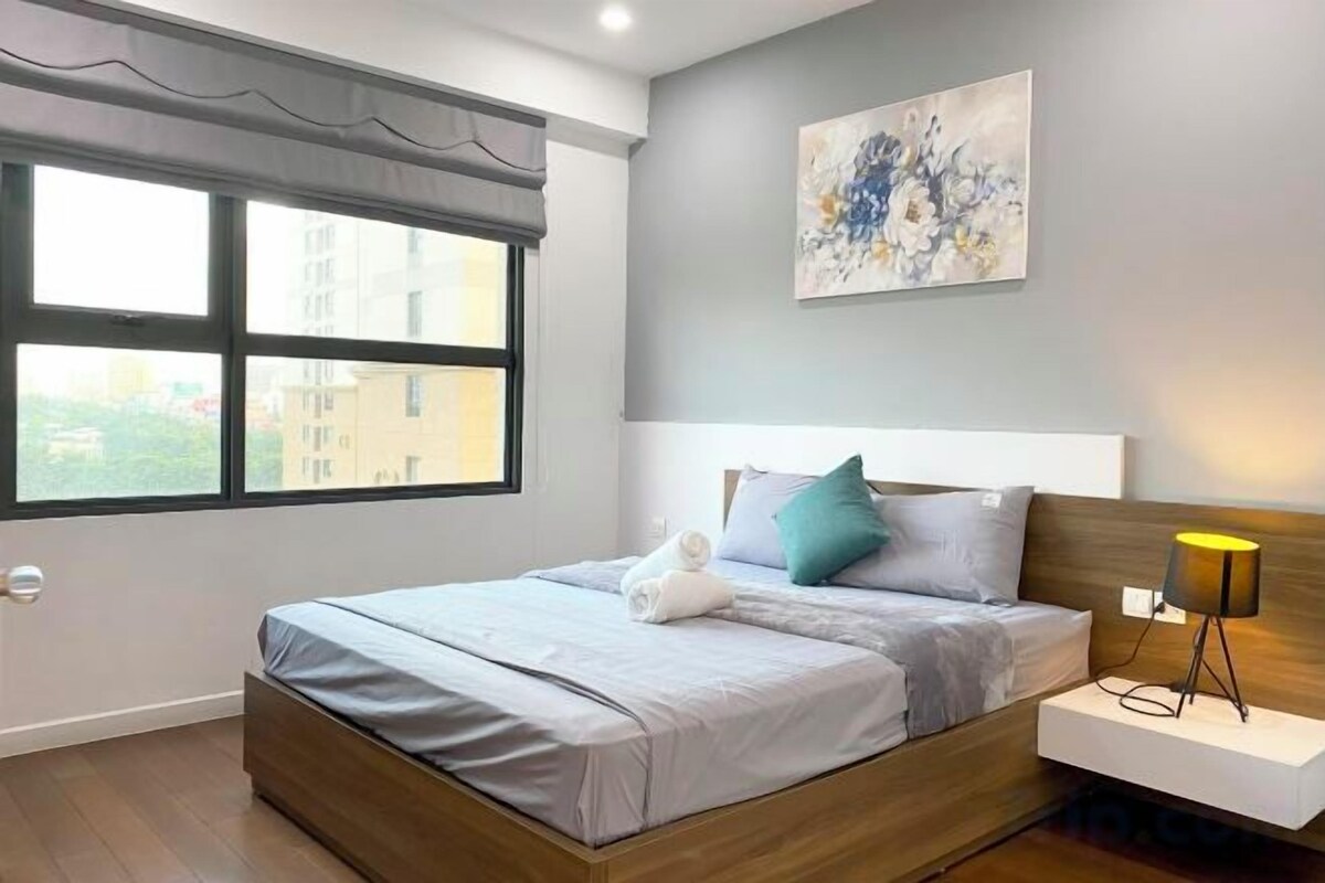 Un dormitorio moderno con cama, mesita de noche, lámpara y una obra de arte en la pared.