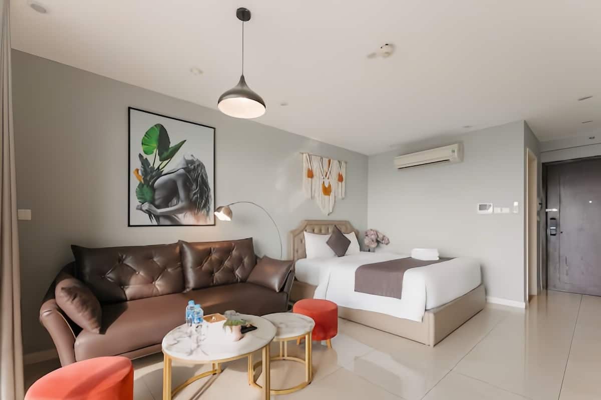 A modern hotel room with a brown leather sofa, a white bed, and a small round table with a red stool.