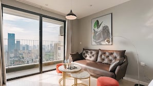 Ein modernes Wohnzimmer mit einem Ledersofa, einem runden Couchtisch und roten Hocker. Ein großes Fenster bietet Blick auf die Stadt.