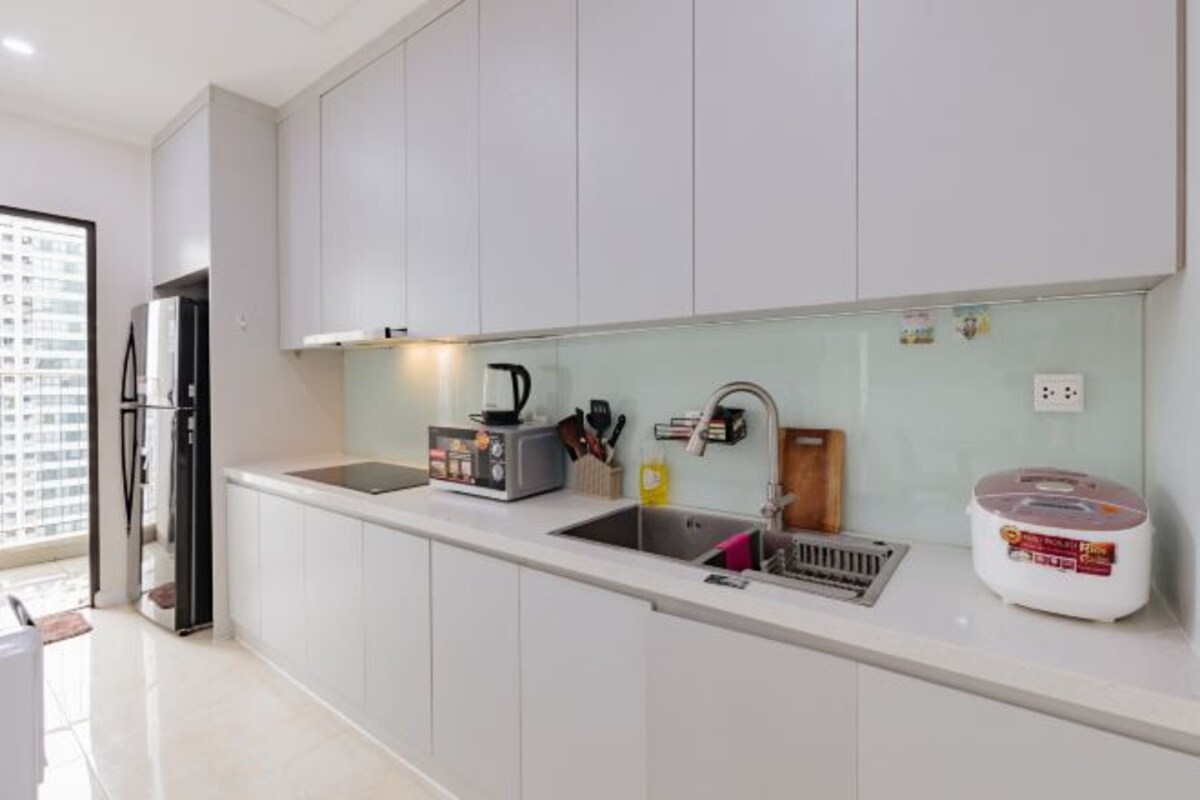 Una cocina moderna con armarios blancos, un lavamanos de acero inoxidable, una cafetera y una cocedora de arroz.