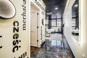 Een moderne hotelgang met een gepoetste vloer, een zithoek met tafels en stoelen, en een grote spiegel aan de muur.