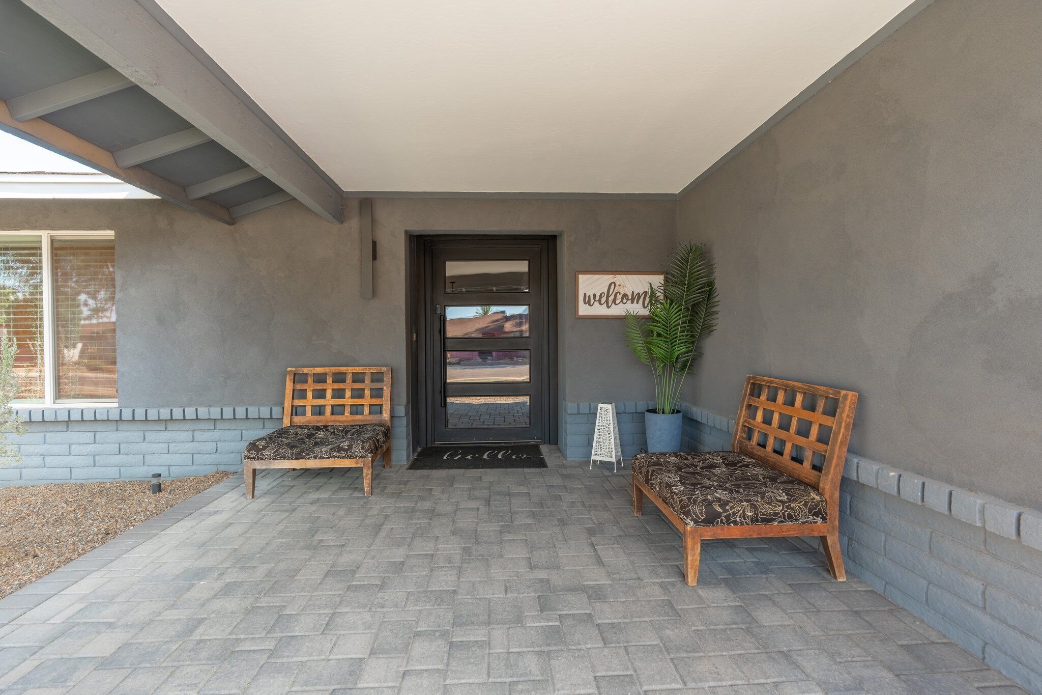 A covered porch with two wooden benches, a welcome sign, and a potted plant.