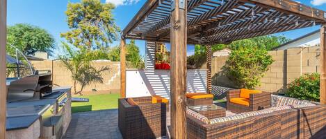 An outdoor patio with a pergola, wicker furniture, and a barbecue grill.