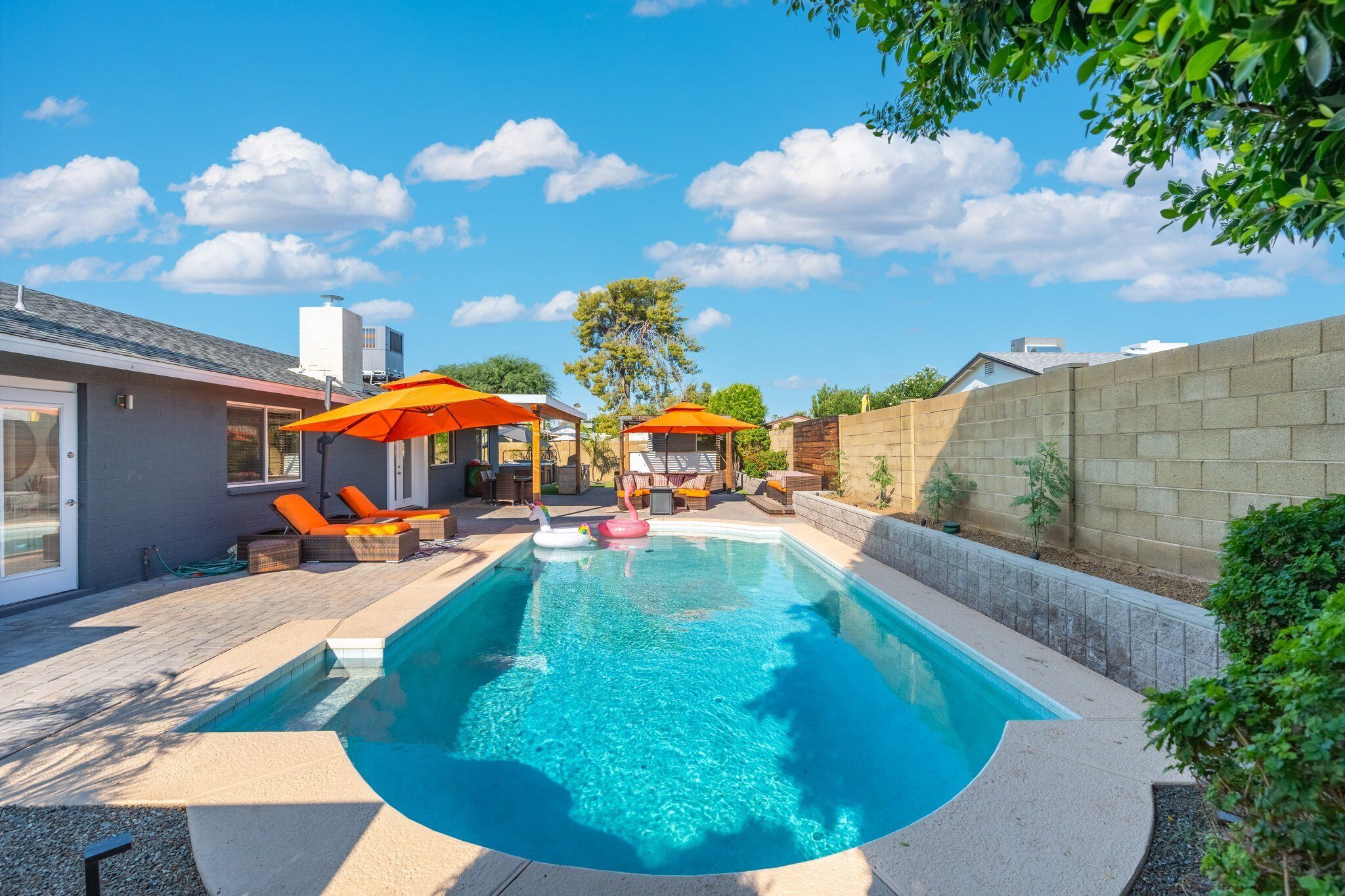 A backyard with a swimming pool, lounge chairs, and umbrellas.
