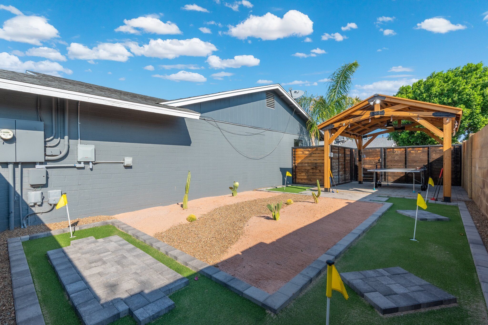 A backyard with a patio, a wooden pergola, and a small garden area with cacti and a flag.
