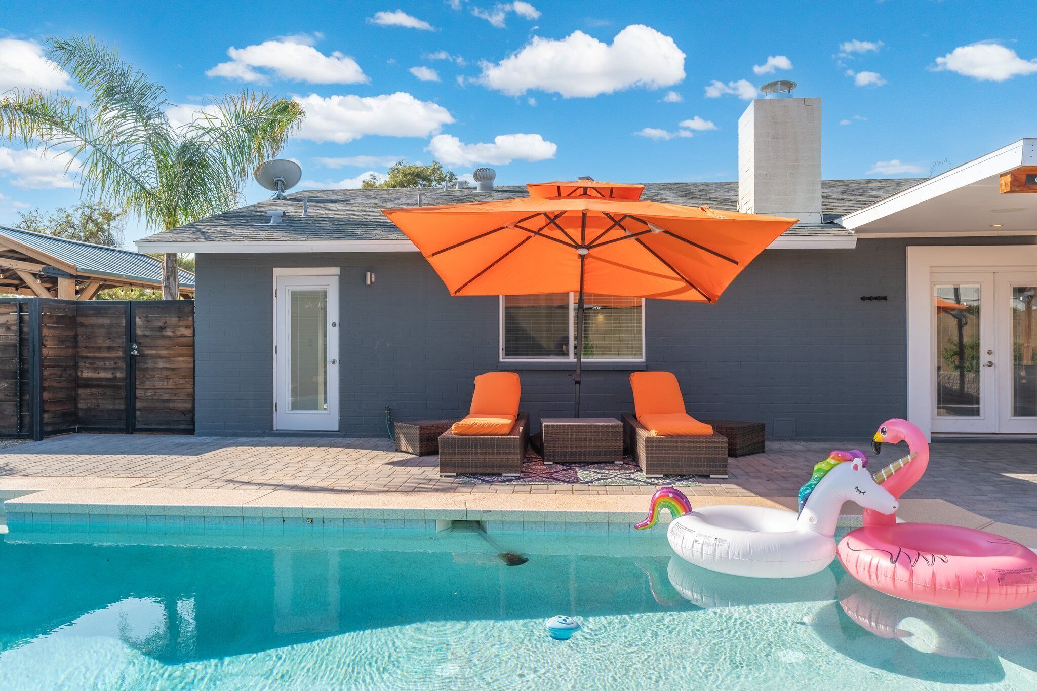 A swimming pool with lounge chairs and an umbrella, a flamingo float, and a unicorn float.