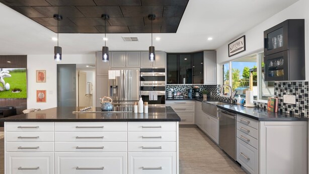 Et moderne køkken med en central ø, rustfrie stålapparater og en backsplash i sort og hvid.