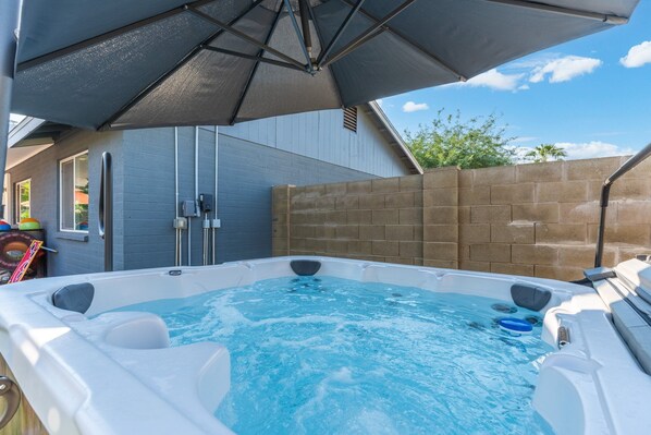 Un jacuzzi con toldo, rodeado por un muro de ladrillo y un edificio azul.