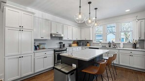 A modern kitchen with white cabinetry, a central island with bar stools, stainless steel appliances, and pendant lighting. - Walk to Five Points | 2 Patios + Private Garage       |     Close to Dining and Bars, Board Games, 10 Mins to Broadway, 24 Hour Hospitality (Nashville)