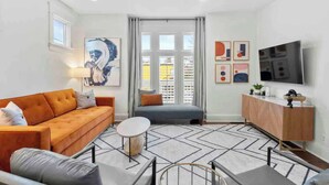 A modern living room with a sofa, a coffee table, a TV, and a cabinet. - Walk to Five Points | 2 Patios + Private Garage       |     Close to Dining and Bars, Board Games, 10 Mins to Broadway, 24 Hour Hospitality (Nashville)