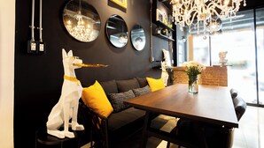 A dining area with a wooden table, black and yellow cushions, a white dog sculpture, and a chandelier.