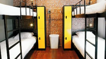 A dormitory room with bunk beds, wooden flooring, and a brick wall.