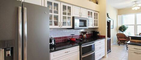 A modern kitchen with stainless steel appliances, white cabinetry, and a red-tiled backsplash.