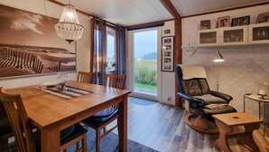 Un coin repas avec une table en bois, des chaises et un lustre. On peut admirer un champ à travers une porte vitrée.
