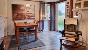 Une pièce chaleureuse avec une table à manger en bois, des chaises, un lustre, un fauteuil en cuir et une table d’appoint.