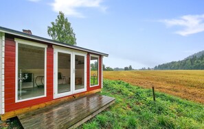 Une cabane rouge avec de grandes fenêtres, une terrasse en bois et une vue sur un champ.