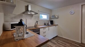 Une cuisine compacte équipée d’un four à micro-ondes, d’une cuisinière et d’un évier. Il y a une fenêtre au-dessus de l’évier et une horloge au mur.