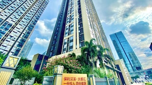 Un edificio alto con varios pisos, rodeado de vegetación y otros edificios modernos.