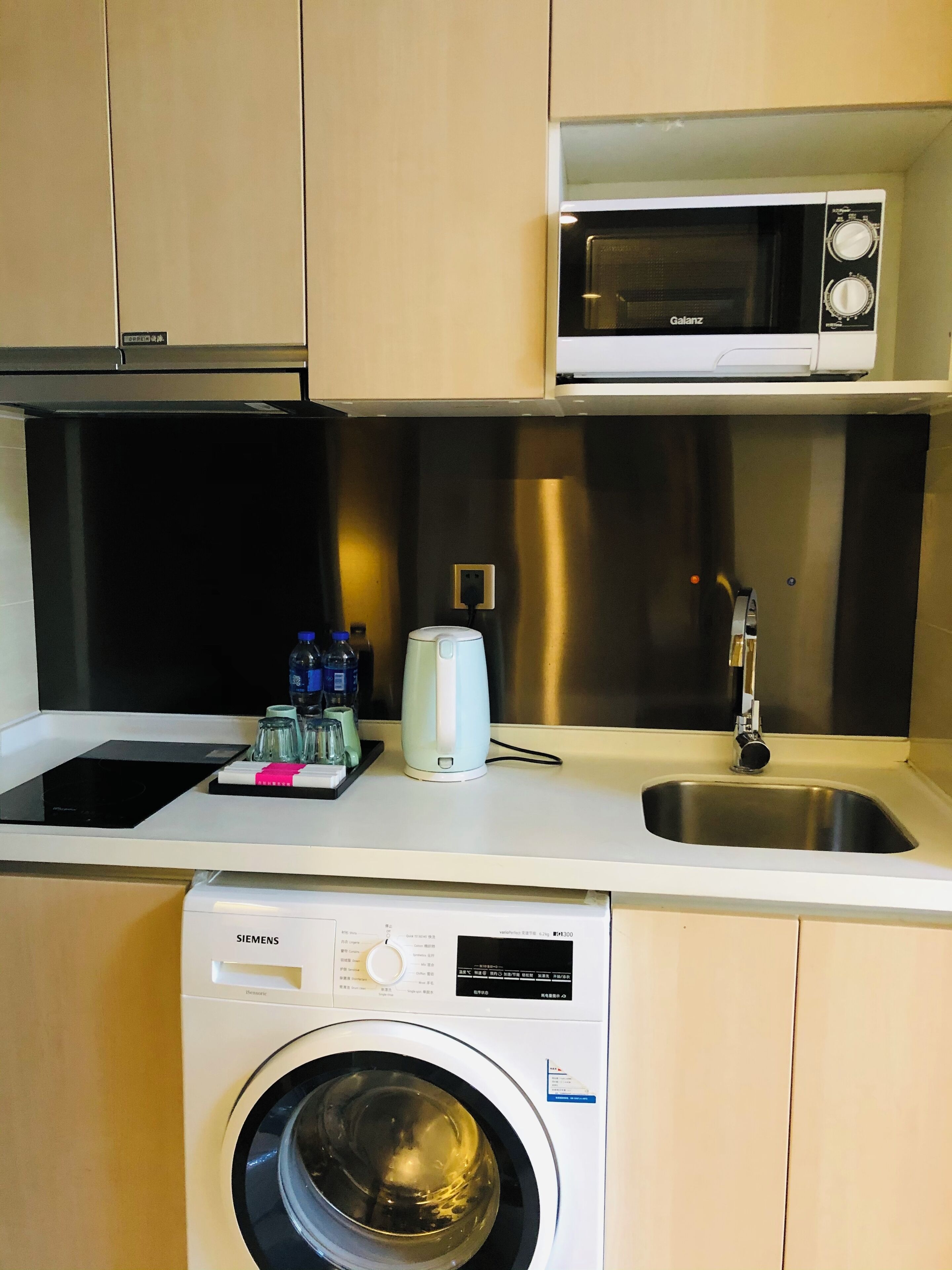 A compact kitchen with a microwave, sink, and washing machine.