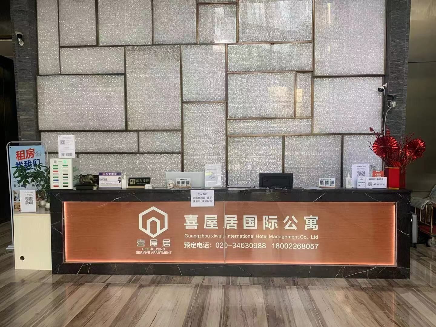 A reception desk with a marble wall backdrop, a sign for HEE Housing Servive Apartment, and a red flower vase.