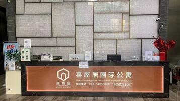 A reception desk with a marble wall backdrop, a sign for HEE Housing Servive Apartment, and a red flower vase.