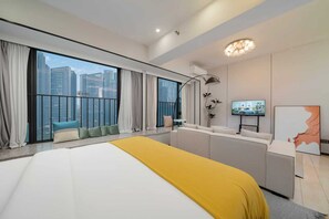Habitación de hotel moderna con una cama grande, un escritorio, un televisor y un balcón con vistas a la ciudad.