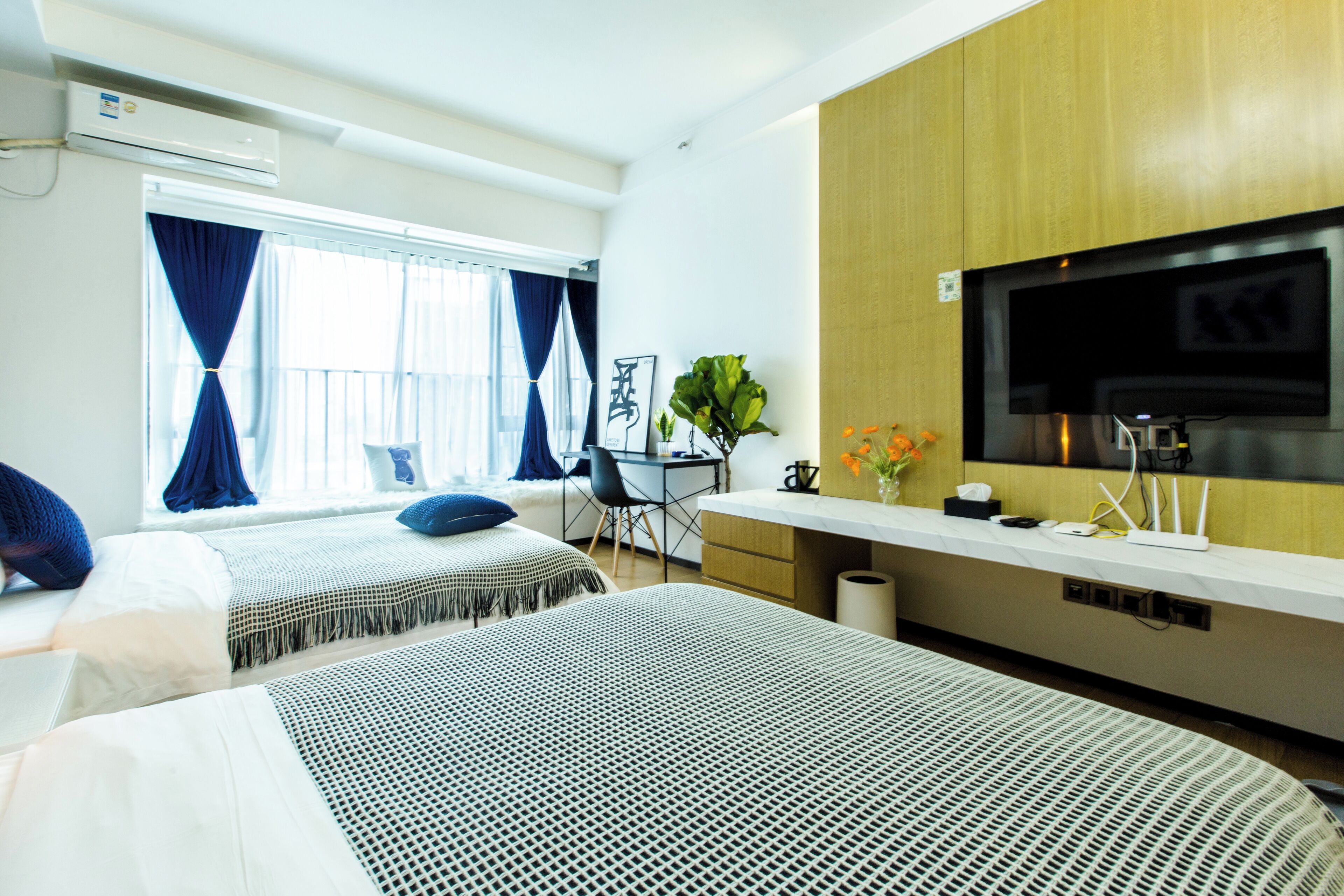 A hotel room with two beds, a desk, a TV, and a window with curtains.