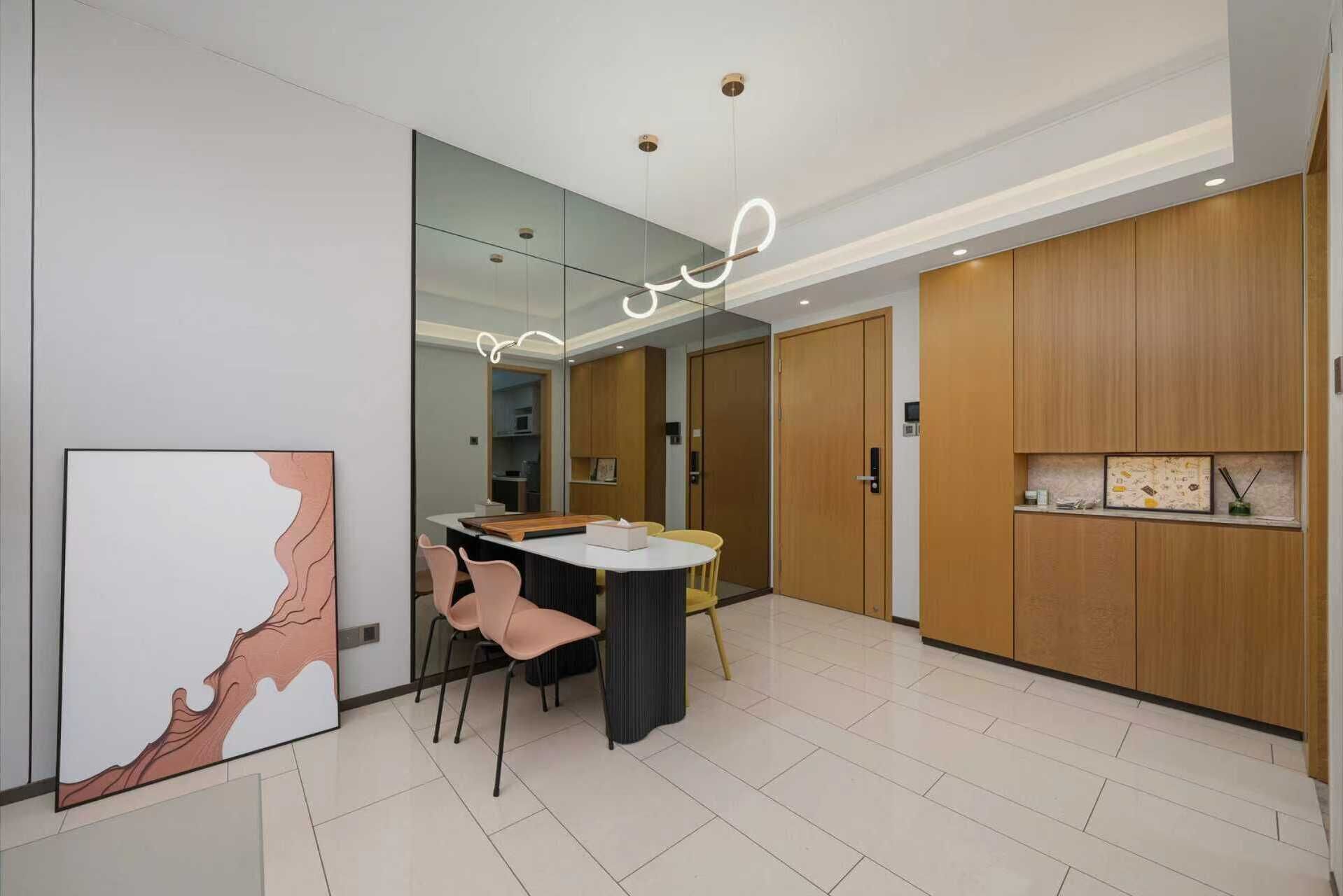 A modern dining area with a round table, two chairs, a large mirror, and wooden cabinets.