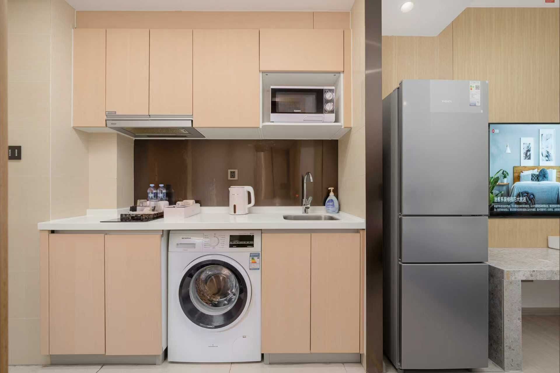 A compact kitchen with a washing machine, a microwave, and a refrigerator.