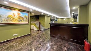 Een lobby met een receptiebalie, een trap en een muurschildering.