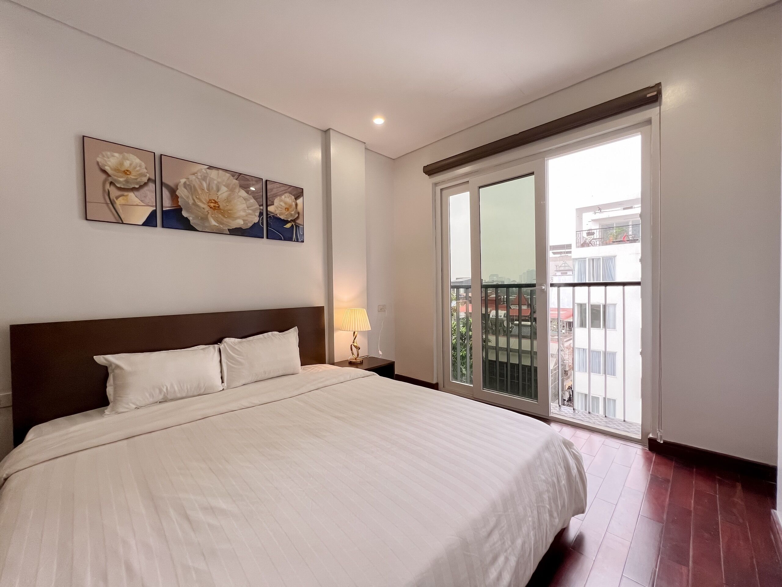 A bedroom with a large bed, a nightstand with a lamp, and a sliding glass door to a balcony.