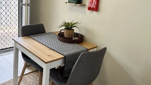 Un comedor con una mesa, sillas y un estante superior con electrodomésticos y recipientes de almacenamiento.