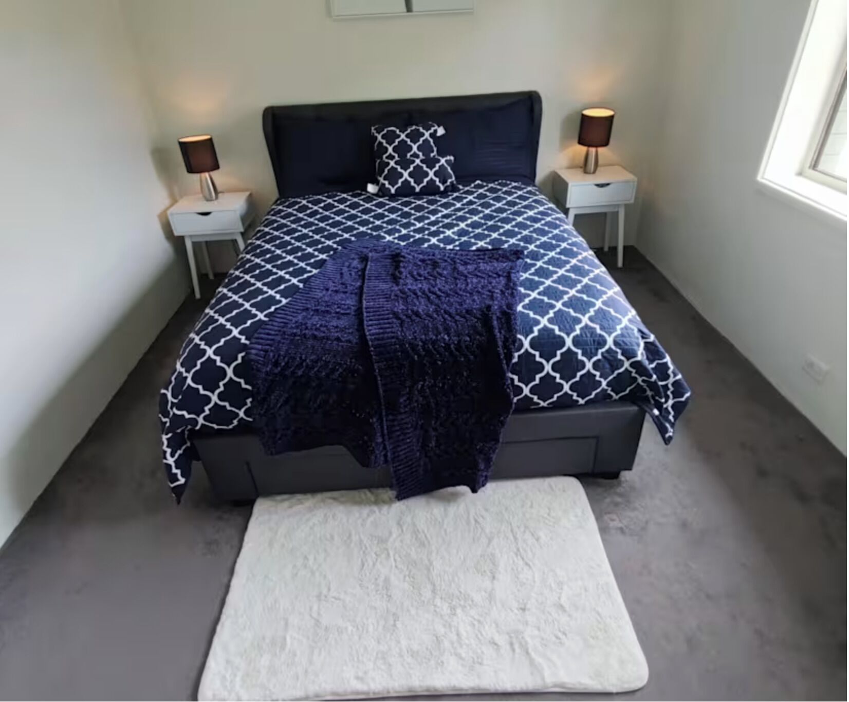 Ein Schlafzimmer mit einem Bett, zwei Nachttischen, einem Fenster und einem weißen Teppich.