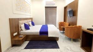 A bedroom with a bed, bedside table, nightstand, and a desk with a chair. - Hotel Shrinath Palace (Mathura)