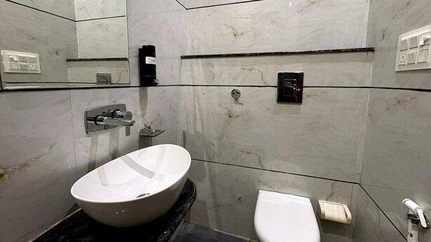 A modern bathroom with a large oval sink, a toilet, and a mirror. - Hotel Shrinath Palace (Mathura)