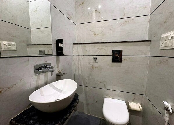 A modern bathroom with a large oval sink, a toilet, and a mirror. - Hotel Shrinath Palace (Mathura)